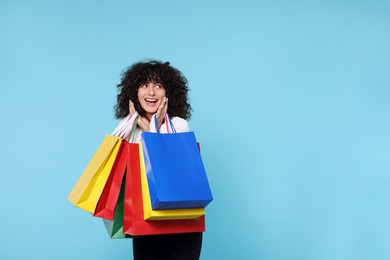 Happy young woman with shopping bags on light blue background. Space for text