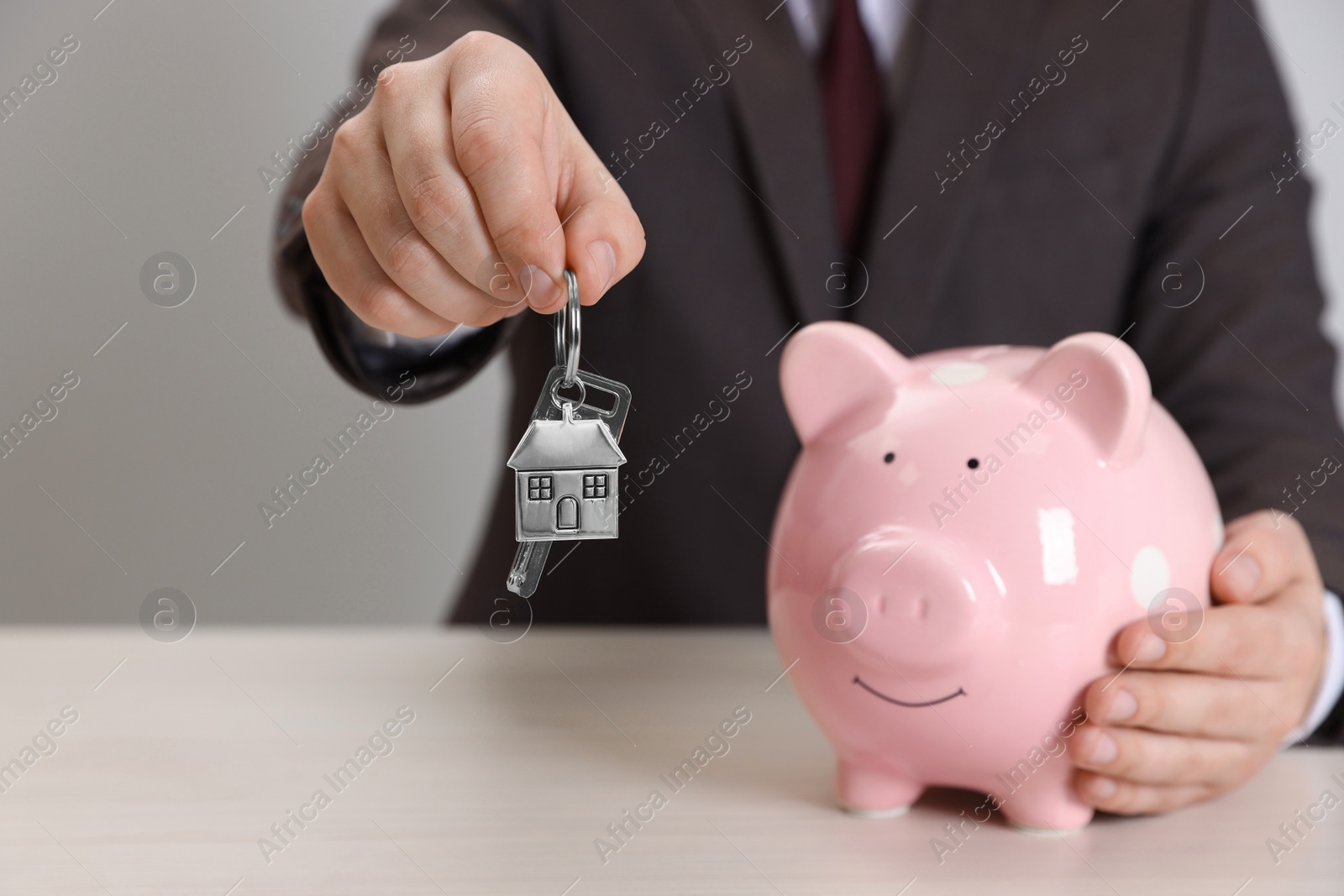 Photo of Man holding key and piggy bank at wooden table, closeup. Saving money for buying house