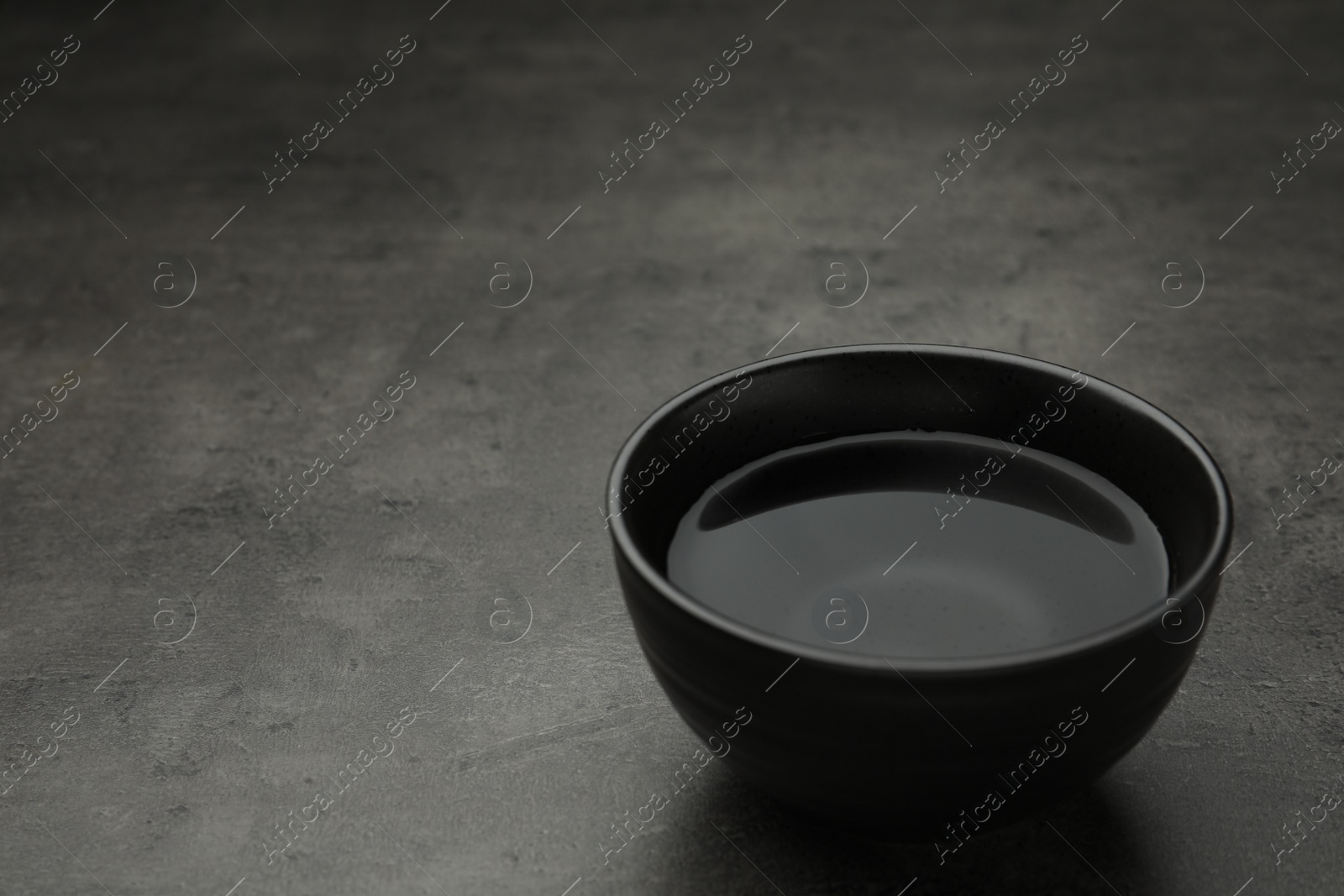 Photo of Black bowl with water on grey table. Space for text