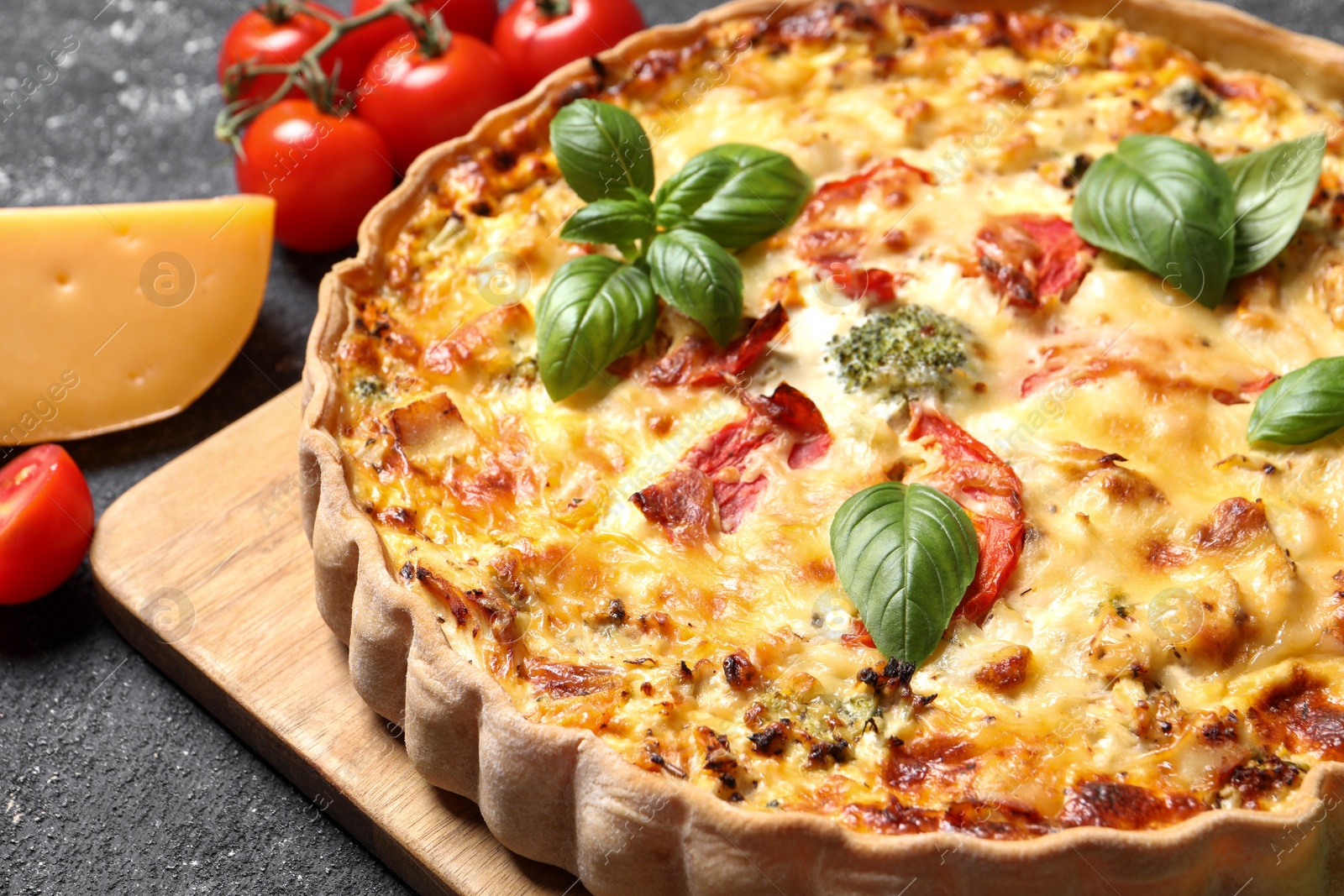 Photo of Tasty quiche with tomatoes, basil and cheese served on dark textured table, closeup