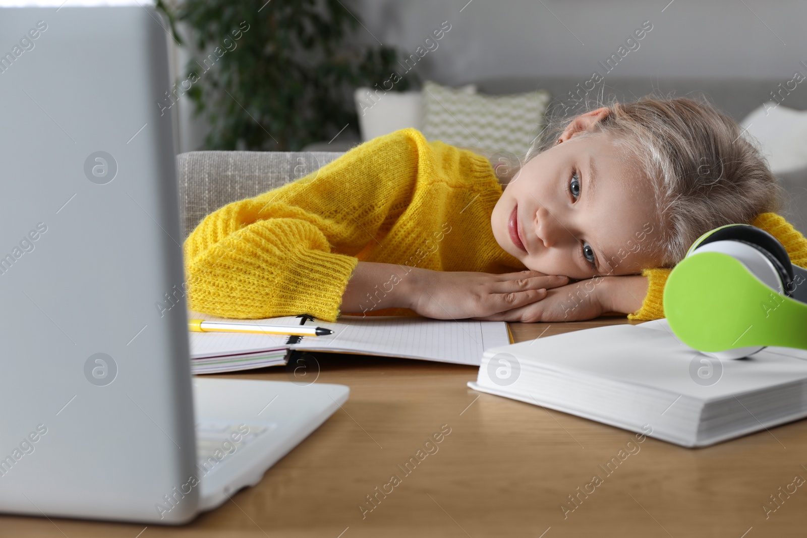 Photo of Cute little girl with modern laptop studying online at home. E-learning