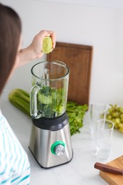 Photo of Woman adding lime juice into blender with ingredients for smoothie in kitchen, closeup