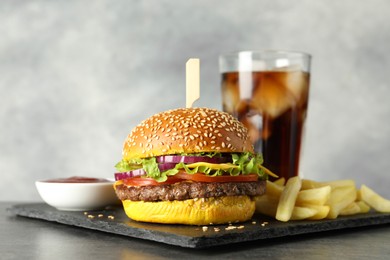 Photo of Burger with delicious patty, soda drink, french fries and sauce on dark table against gray background, closeup