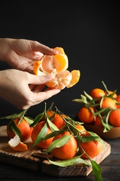 Woman peeling ripe tangerine over table on dark background, closeup