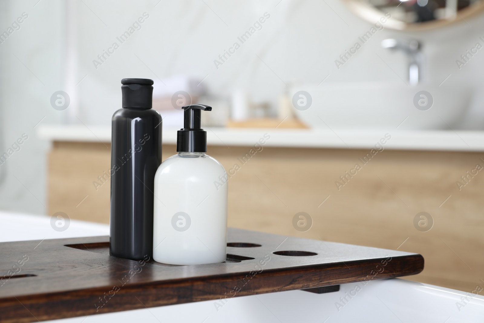 Photo of Wooden bath tray with bottles of shower gels on tub indoors, space for text