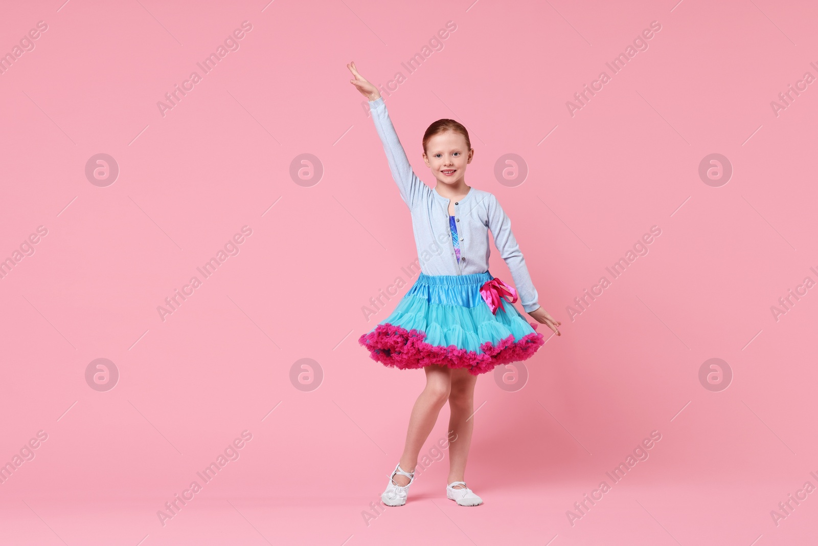 Photo of Cute little girl dancing on pink background