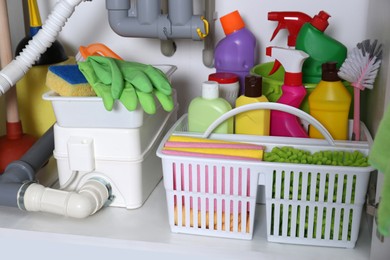 Photo of Open under sink cabinet with different cleaning supplies in kitchen