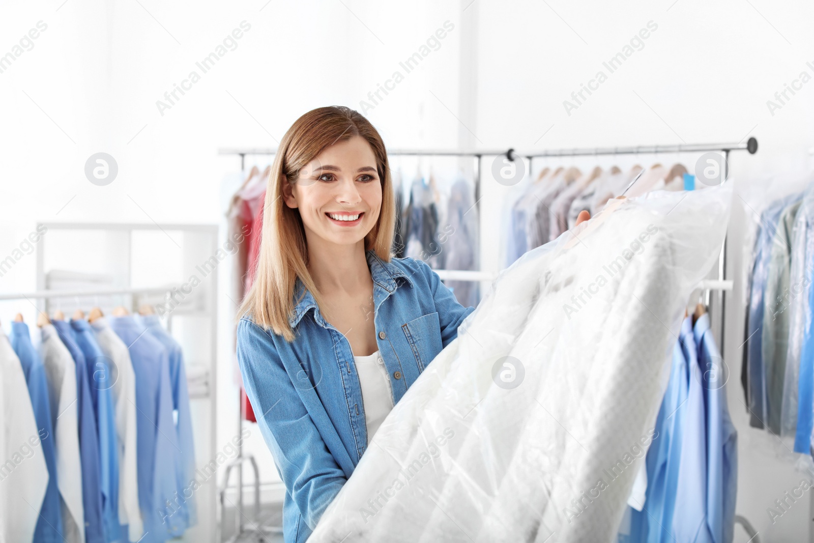 Photo of Young woman holding hanger with clothes in plastic bag at dry-cleaner's