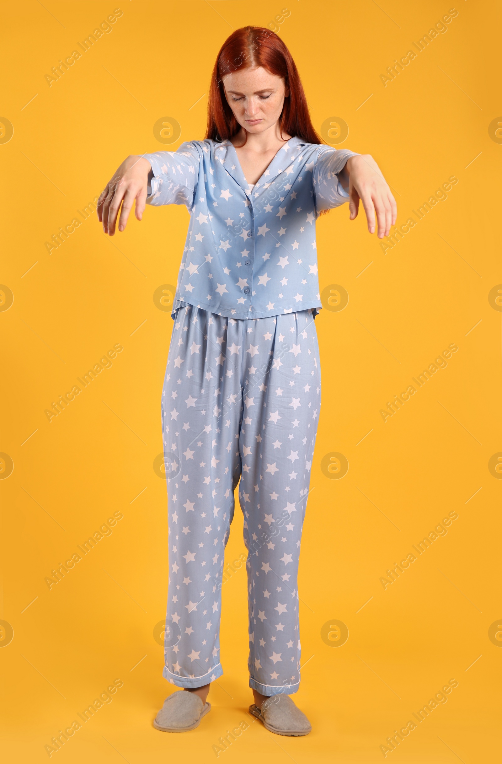 Photo of Young woman wearing pajamas and slippers in sleepwalking state on yellow background