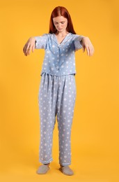 Photo of Young woman wearing pajamas and slippers in sleepwalking state on yellow background