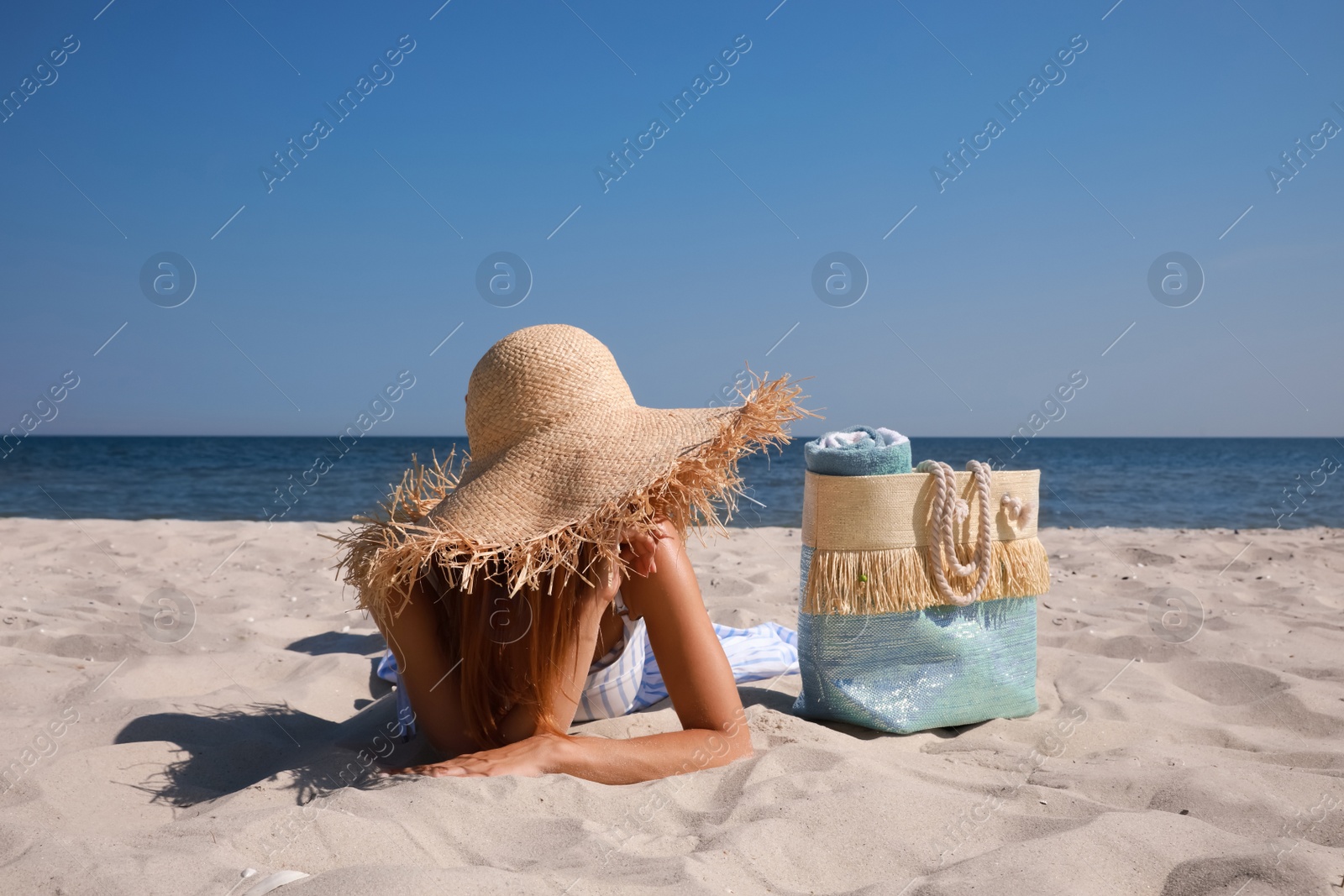 Photo of Woman with beach bag and straw hat lying on sand near sea