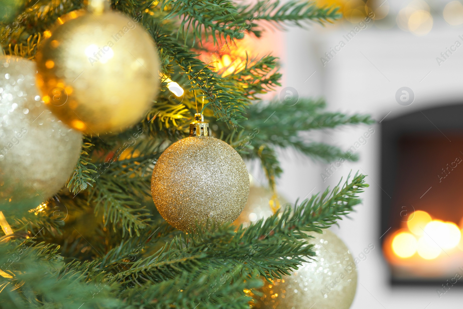 Photo of Beautiful golden Christmas balls hanging on fir tree branch against blurred background, closeup