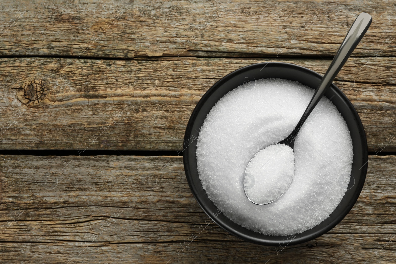 Photo of Granulated sugar in bowl and spoon on wooden table, top view. Space for text