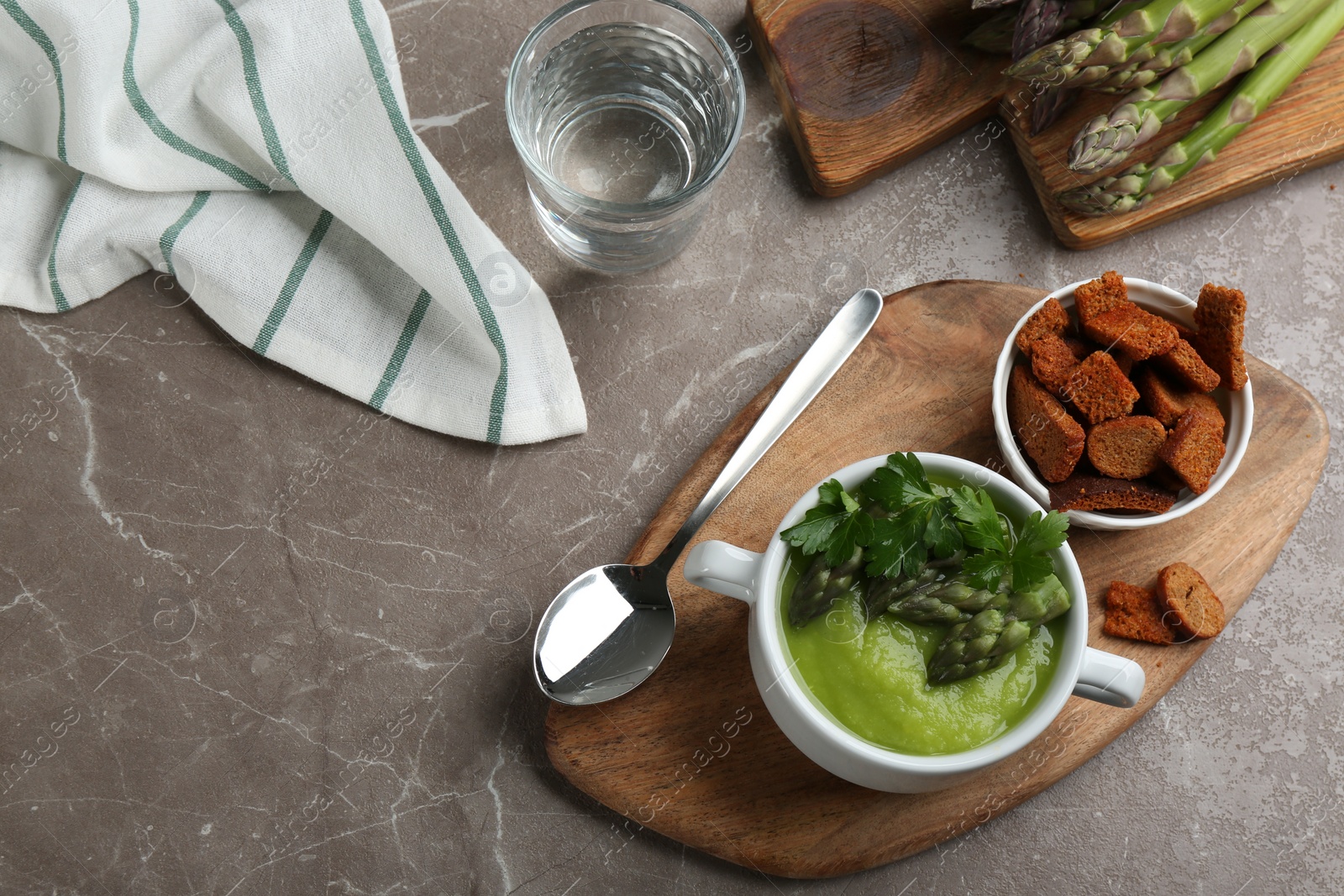 Photo of Delicious asparagus soup served on grey marble table, flat lay