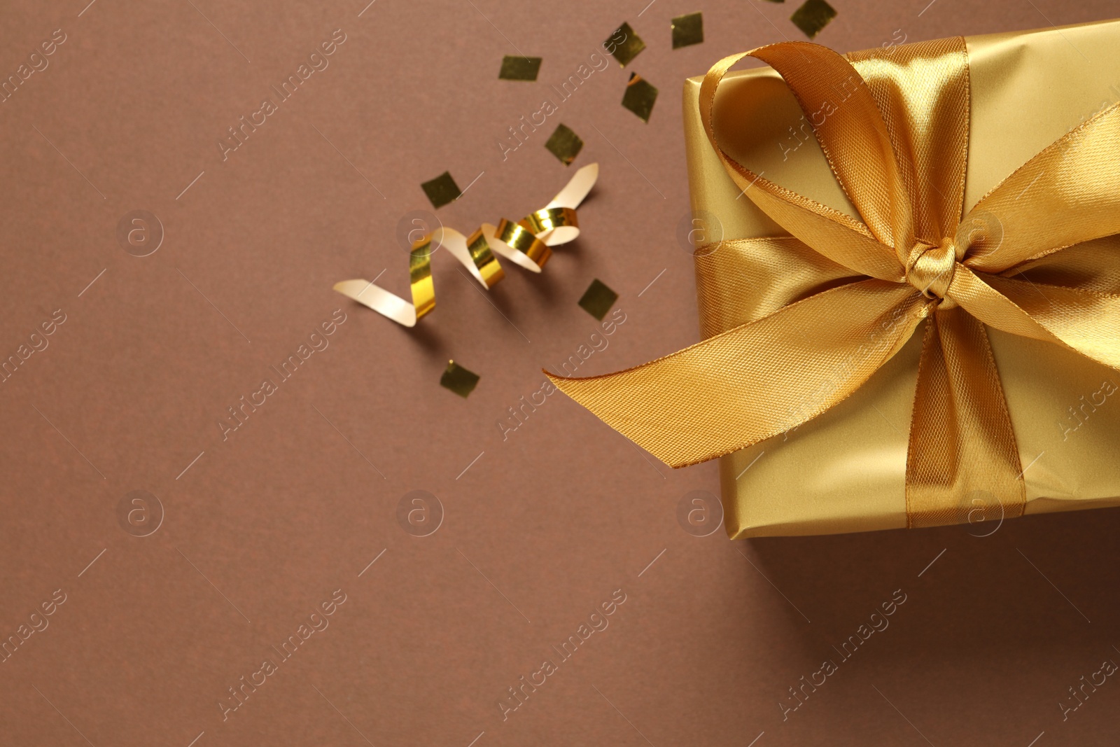 Photo of Beautiful golden gift box and confetti on brown background, flat lay. Space for text