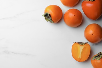 Photo of Delicious ripe persimmons on white marble table, flat lay. Space for text