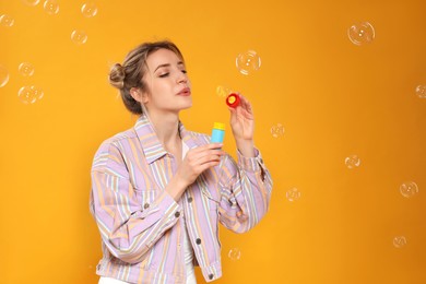 Photo of Young woman blowing soap bubbles on yellow background, space for text