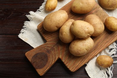 Photo of Raw fresh potatoes and cutting board on wooden table, top view