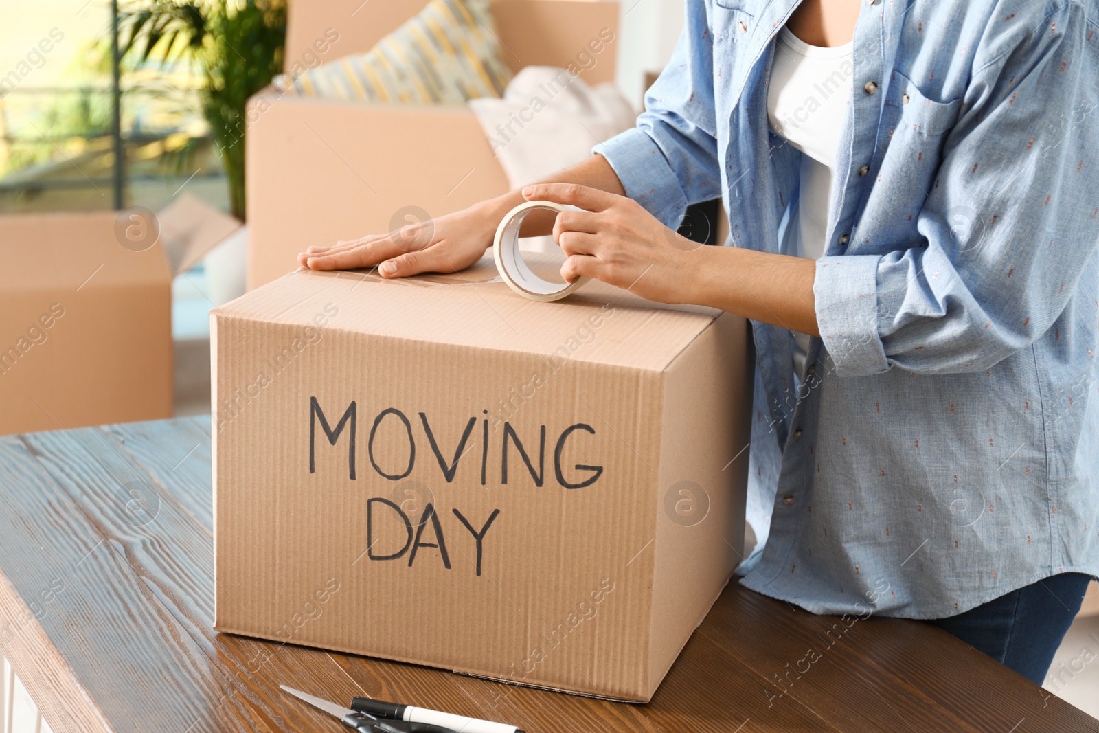 Photo of Woman packing box with words MOVING DAY at wooden table, closeup