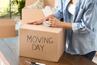 Photo of Woman packing box with words MOVING DAY at wooden table, closeup