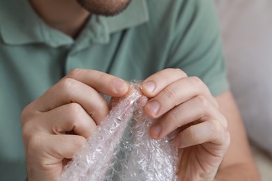 Man popping bubble wrap indoors, closeup view. Stress relief