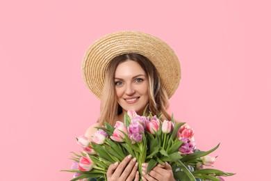 Photo of Happy young woman in straw hat holding bouquet of beautiful tulips on pink background