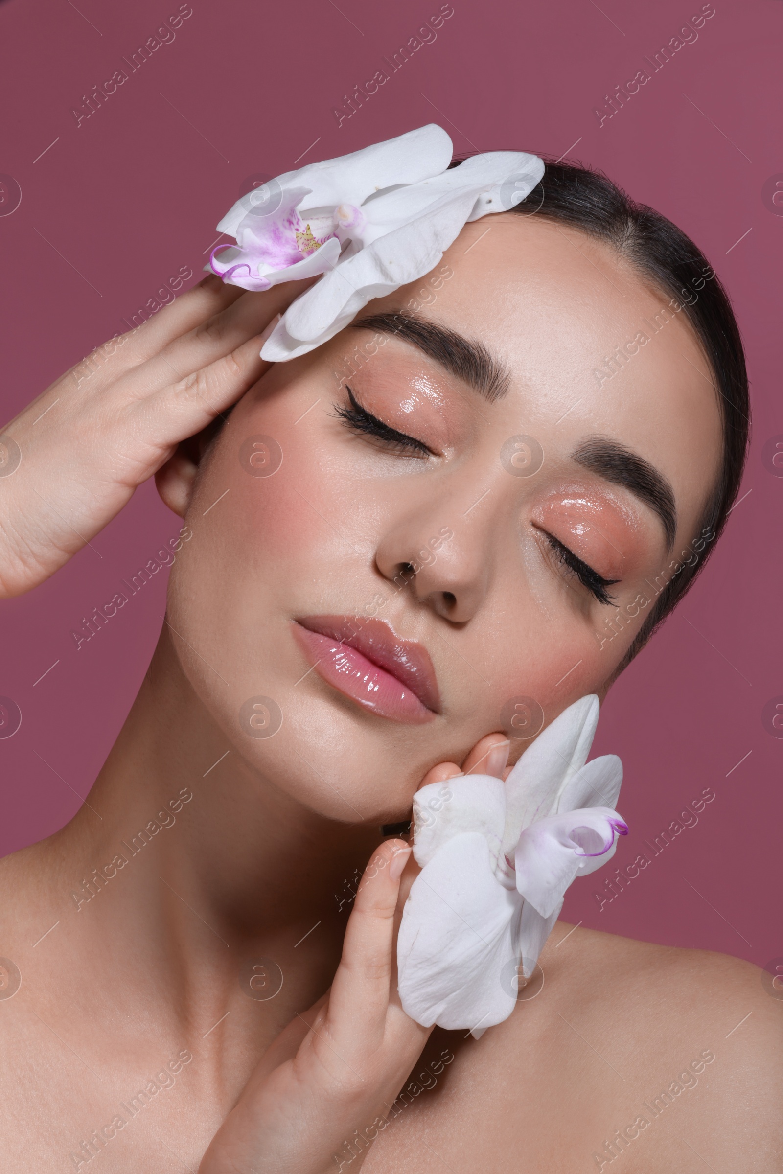 Photo of Portrait of beautiful young woman with orchid flowers on dark pink background, closeup