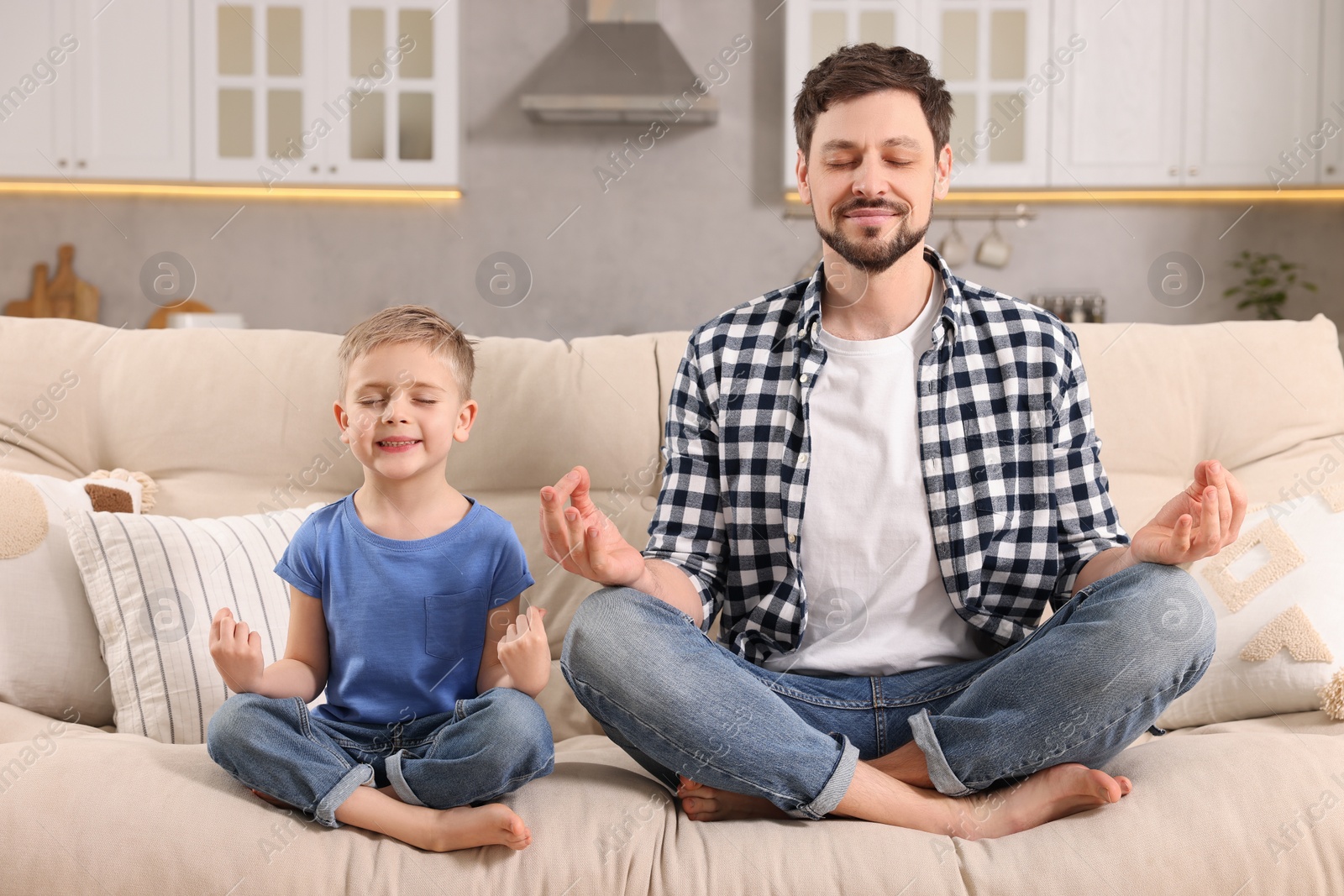 Photo of Father with son meditating together on sofa at home. Harmony and zen