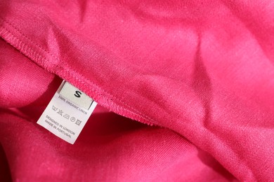 Clothing label in different languages on pink garment, closeup