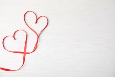 Photo of Hearts made of red ribbon on white wooden background, top view with space for text. Valentine's day celebration