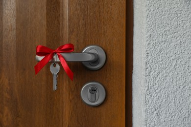 Photo of House key with red bow on door handle, closeup. Housewarming party