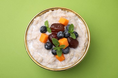 Delicious barley porridge with blueberries, pumpkin, dates and mint in bowl on green table, top view