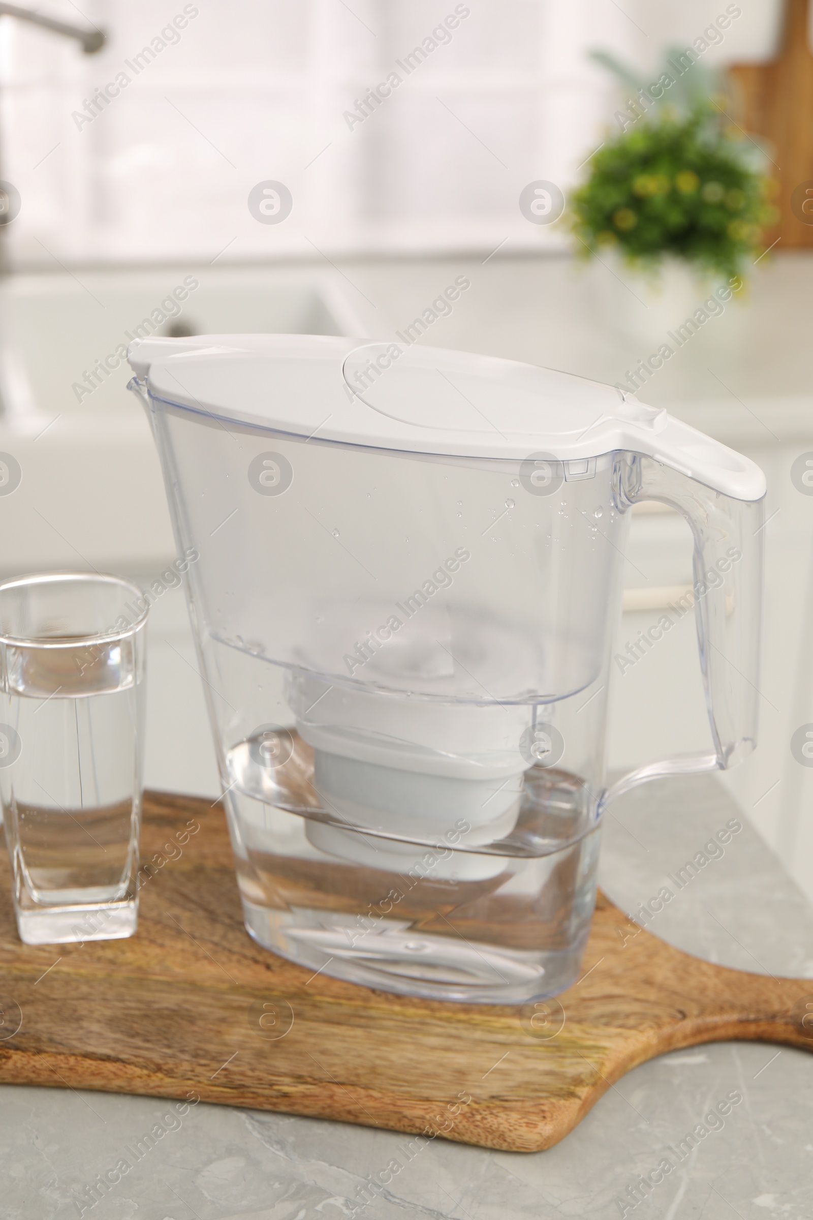 Photo of Water filter jug and glass on light table in kitchen, closeup