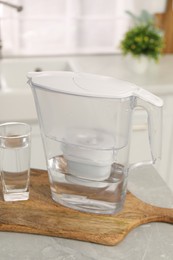 Photo of Water filter jug and glass on light table in kitchen, closeup