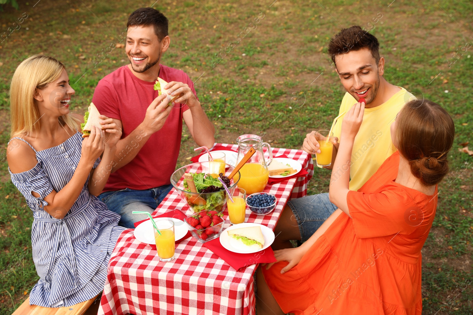 Photo of Group of people having picnic at table in park on summer day