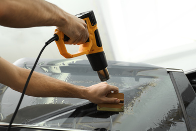 Photo of Worker tinting car window with heat gun in workshop, closeup