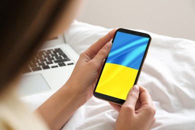 Woman holding smartphone with Ukrainian national flag on screen indoors, closeup