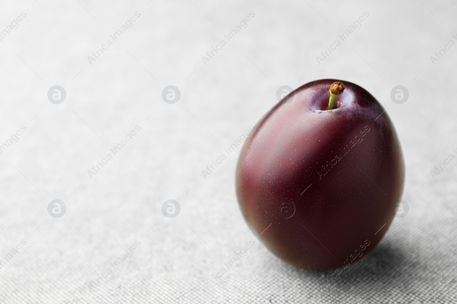 Photo of Tasty ripe plum on light fabric, closeup. Space for text