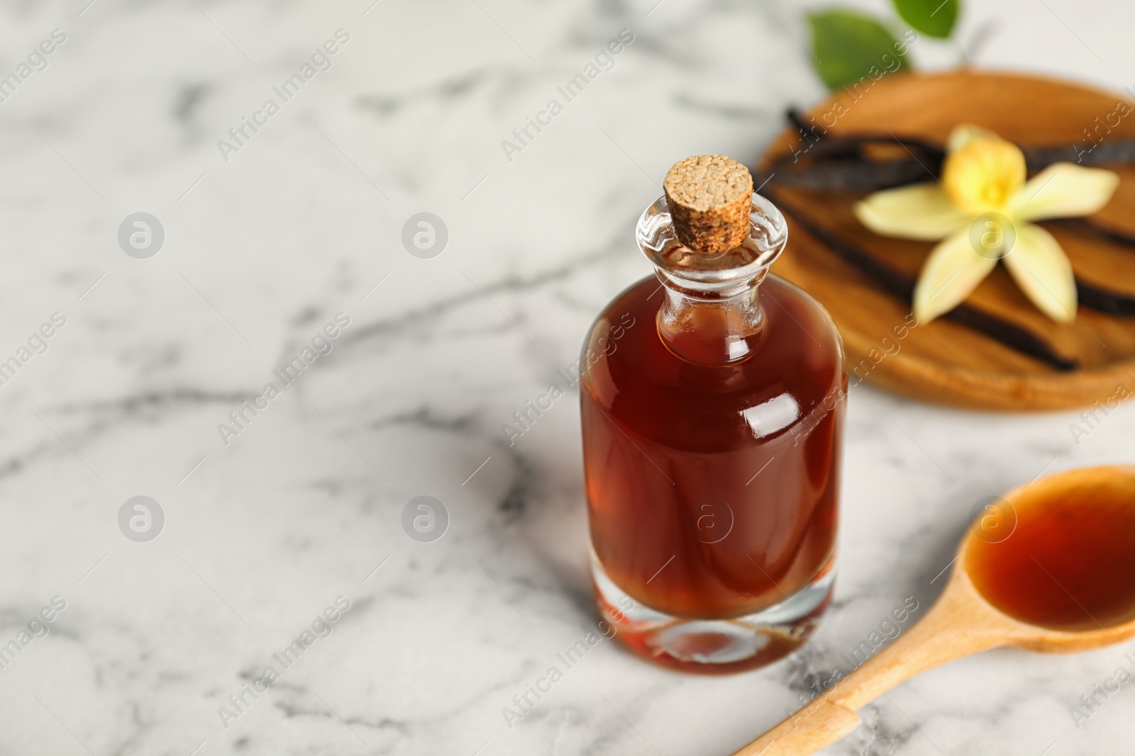 Photo of Aromatic homemade vanilla extract on marble table, closeup. Space for text