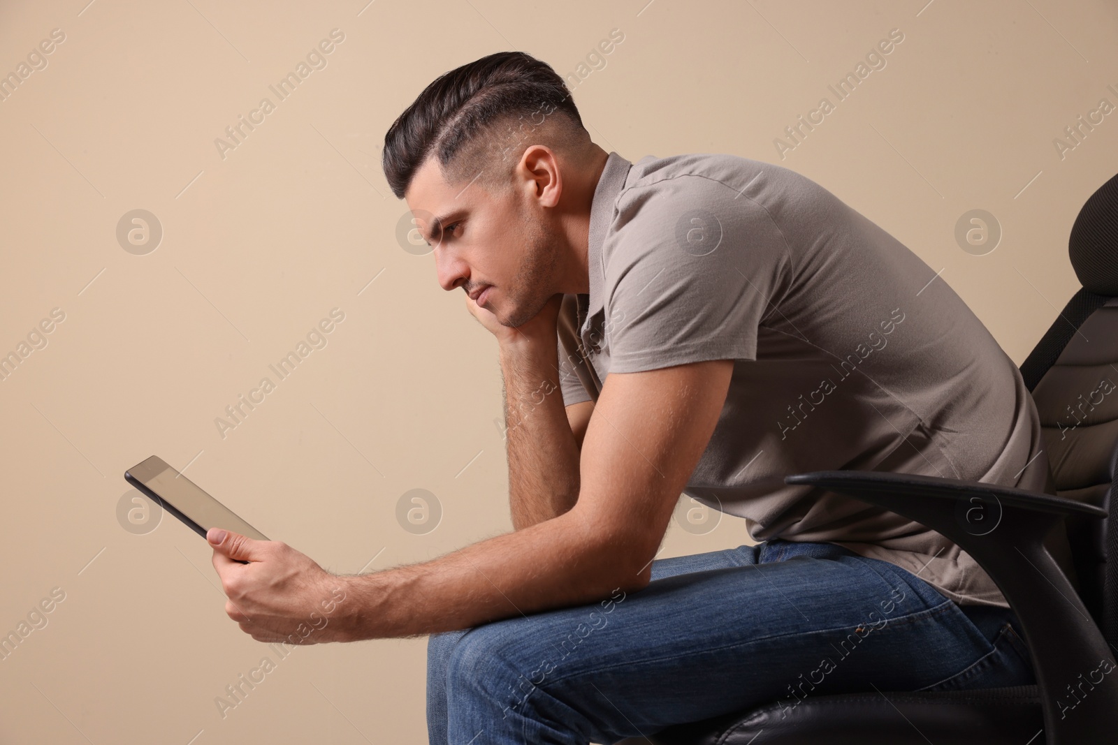 Photo of Man with poor posture using tablet while sitting on chair against beige background