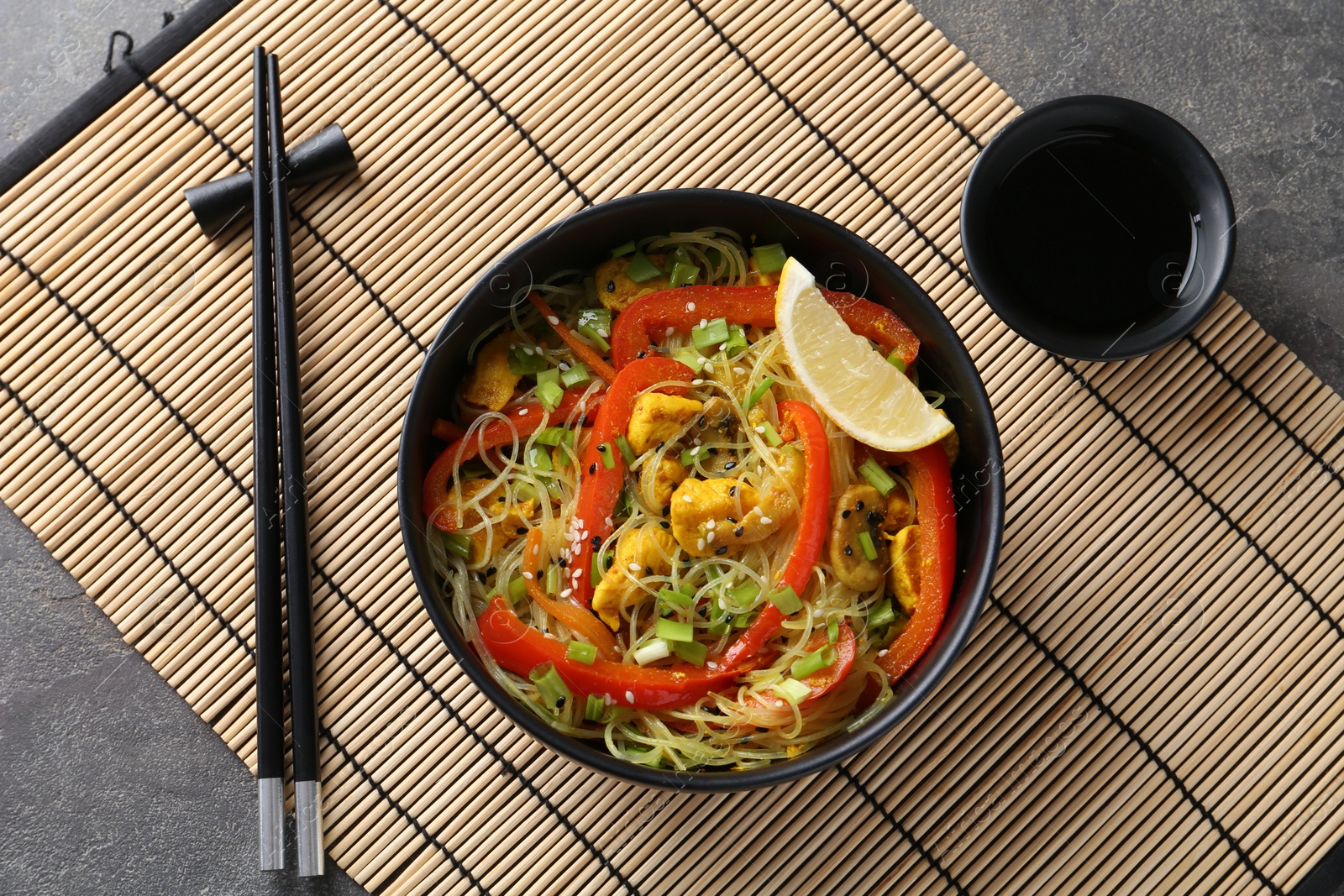 Photo of Stir-fry. Delicious cooked noodles with chicken and vegetables in bowl served on gray textured table, flat lay