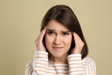 Young woman suffering from migraine on beige background