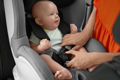 Photo of Mother fastening baby to child safety seat inside of car