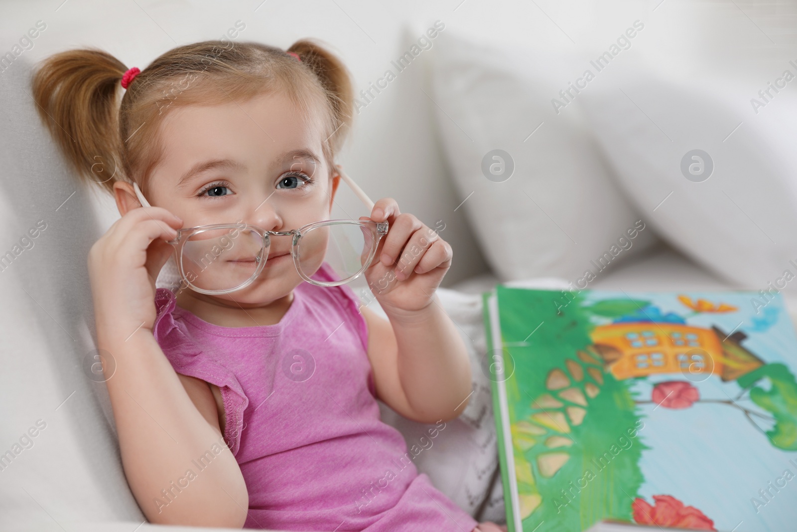 Photo of Cute little girl with book on sofa at home