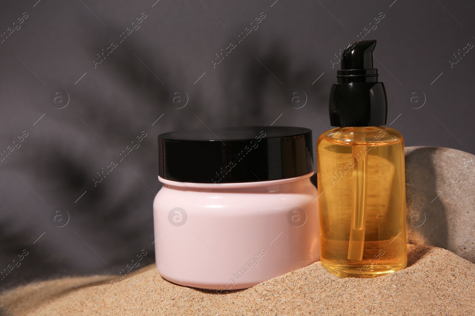 Photo of Cosmetic products and stone on sand against grey background. Space for text