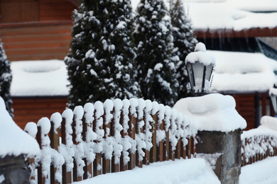 Fence near cottage covered with snow outdoors on winter day