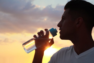 Photo of Man drinking water to prevent heat stroke outdoors at sunset