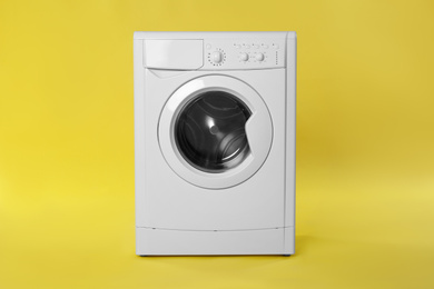 Photo of Modern washing machine on yellow background. Laundry day