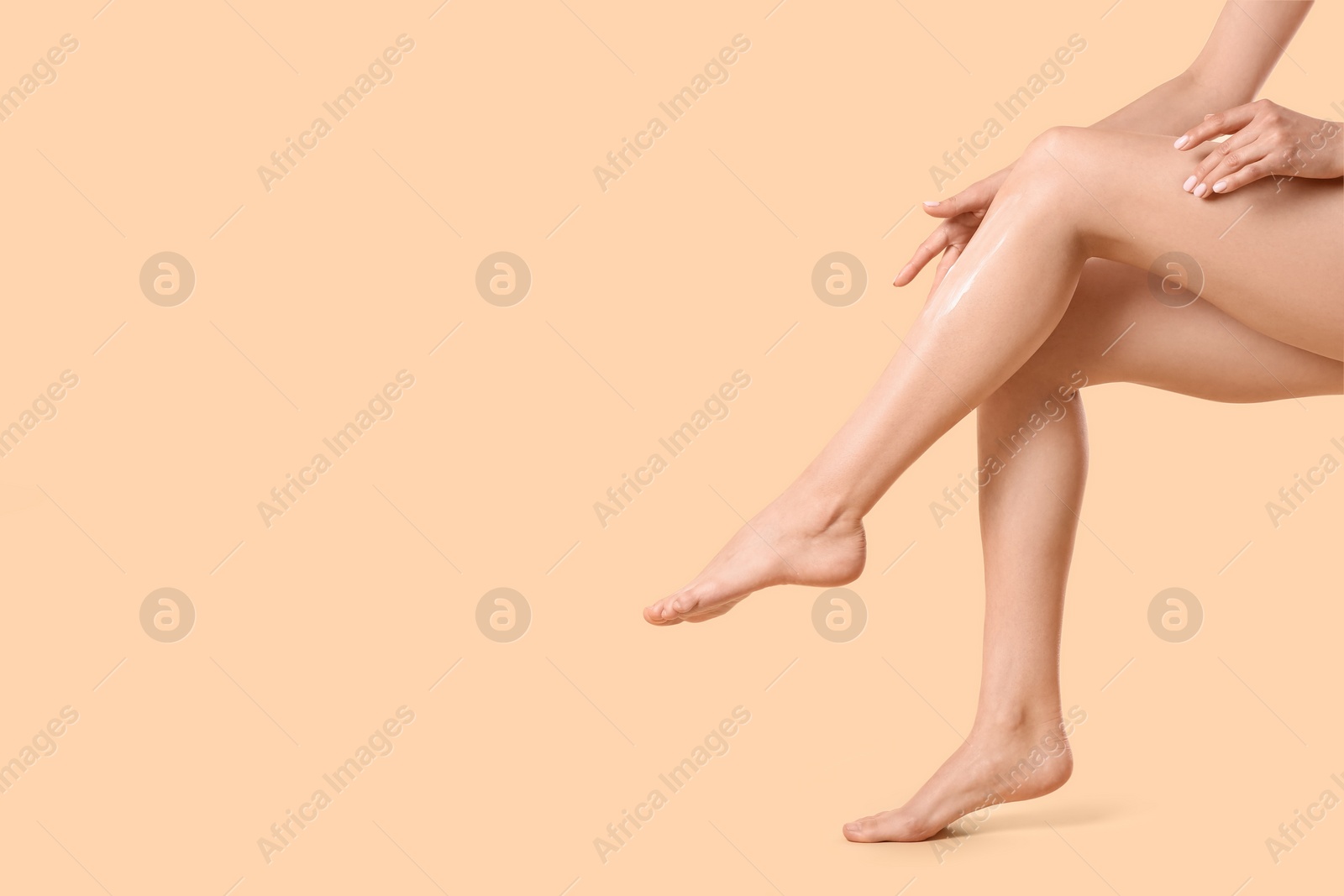 Photo of Woman applying body cream onto her smooth legs on beige background, closeup. Space for text