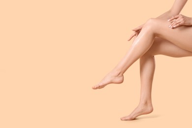 Photo of Woman applying body cream onto her smooth legs on beige background, closeup. Space for text